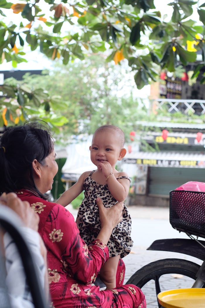 Smiling baby in leopard print dress being held by an adult woman outdoors.