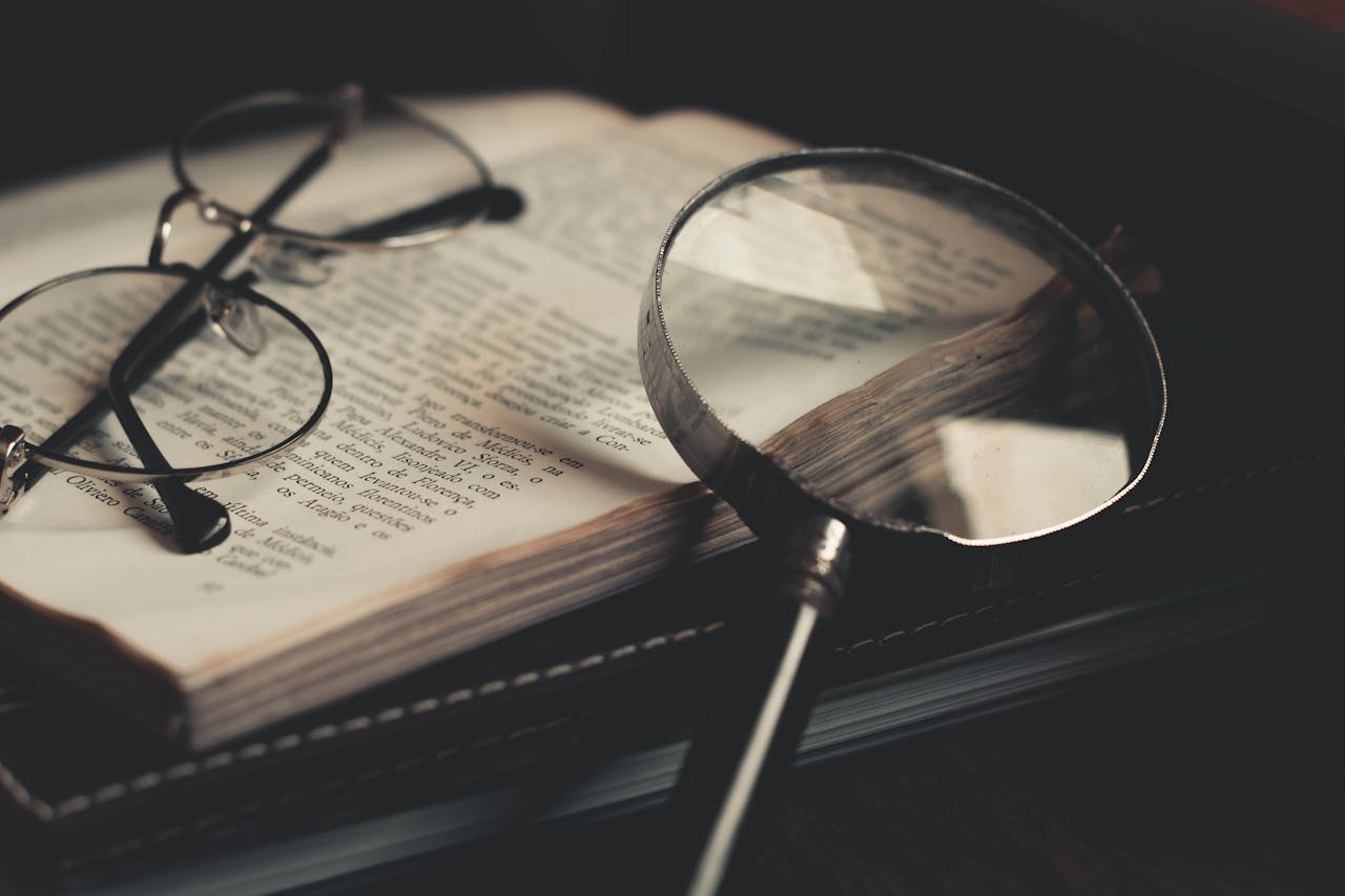 Detailed close-up of an open book with a magnifying glass and eyeglasses, emphasizing discovery and exploration.